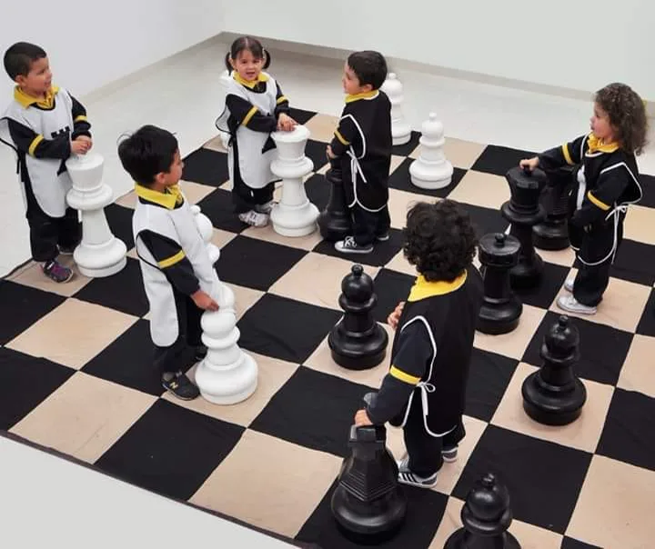 Niños en uniforme jugando sobre un tablero de ajedrez gigante con piezas de tamaño real